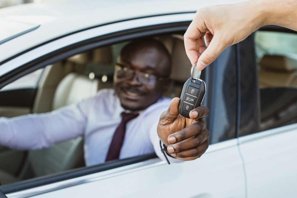 Happy customer sitting in car, receiving car key from dealer's hand.