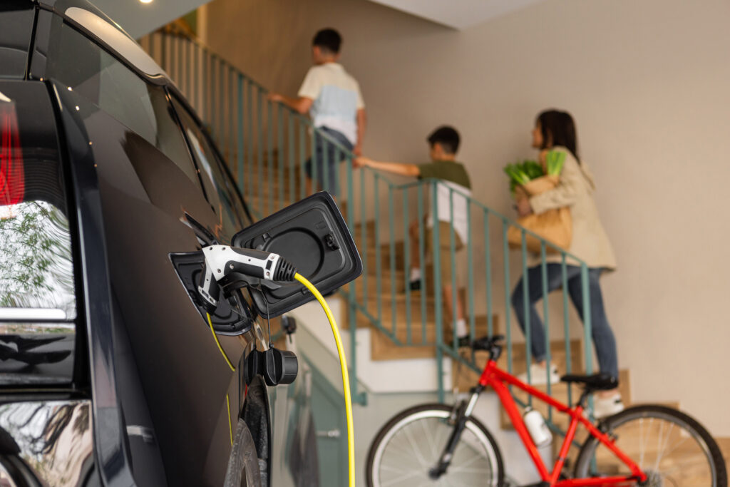 Electric vehicle charging in a garage with a family of 3 going up the stairs in the background.